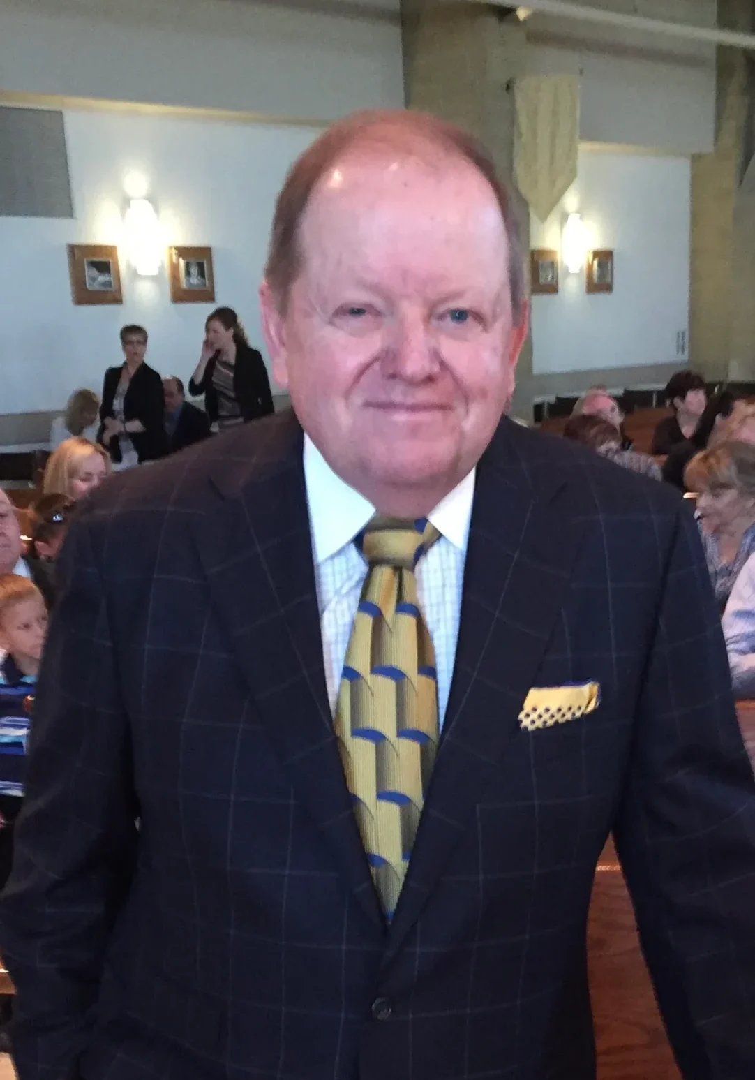 A man in a suit and tie standing next to a crowd.